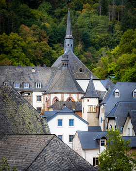 European village nestled in forested hills with stone church steeple rising prominently above residential buildings.