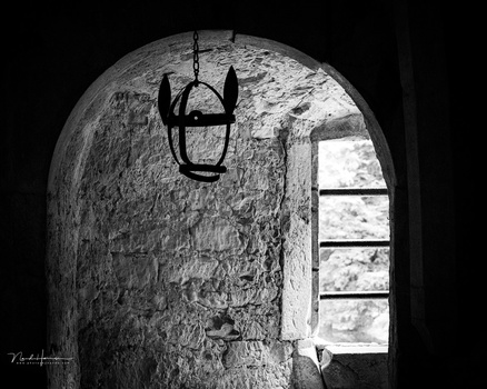 Iron chandelier hanging in a curved stone archway with a narrow window overlooking landscape.