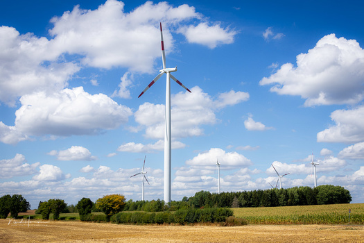 Wind turbines in a rural agricultural landscape under partly cloudy skies.