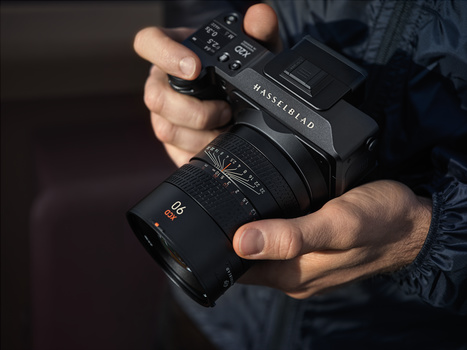 Photographer's hands holding a Hasselblad medium format camera with attached lens.