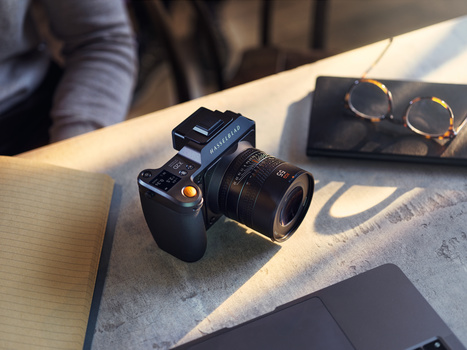Camera with lens and external flash on wooden surface with eyeglasses and notebook nearby.
