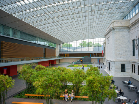 Modern indoor courtyard with glass ceiling, bamboo plants, and colorful architectural elements.