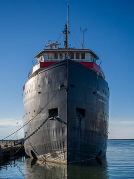 Large commercial vessel with red and white superstructure docked at a pier under clear blue sky.