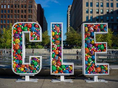 Large colorful ball-filled letters spelling 'OLE' in an urban plaza surrounded by tall buildings.