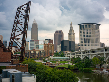 Urban skyline with historic bridge, river, and mix of architectural styles under cloudy sky.