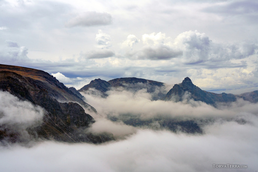 Mountain peaks partially shrouded in low clouds and mist beneath a dramatic cloudy sky.