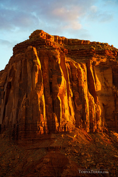 Red rock formation illuminated by warm golden sunlight during sunset or sunrise.