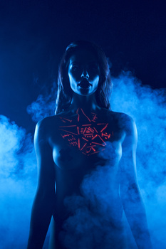 Woman silhouetted against blue volumetric lighting with a glowing geometric symbol on her chest.