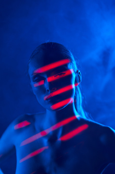 Portrait of a person with horizontal red light streaks across their face and torso against a blue background.