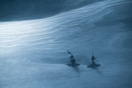 Two sailing ships on calm blue water viewed from above, with light reflecting across the surface.