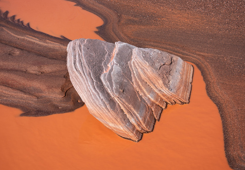 Aerial view of white rock formation surrounded by vibrant orange mineral-stained water and brown earth.