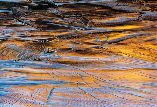 Layered rock formations with blue and golden-orange mineral striations and flowing patterns.
