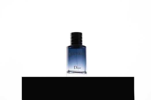 Blue glass fragrance bottle with black cap centered on white background above black bar.