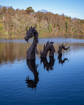 Three wooden dragon sculptures emerging from calm water with forested shoreline in background.