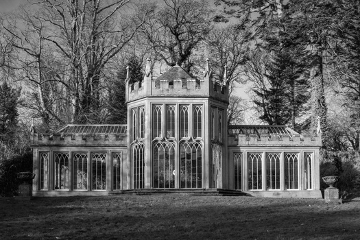 Gothic Revival stone structure with central tower and symmetrical wings, bare trees surrounding.
