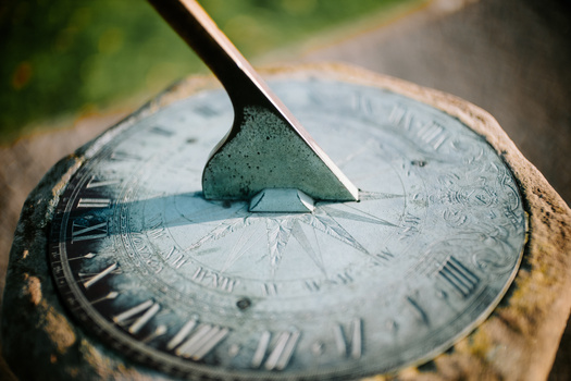 Weathered sundial with shadow cast by metal gnomon, showing patina and aged surface texture.