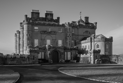 A grand castle with multiple towers and chimneys photographed in black and white against an overcast sky.
