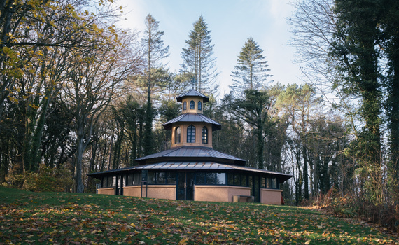 Octagonal pavilion with peach-colored walls and dark roof set among bare trees in autumn.