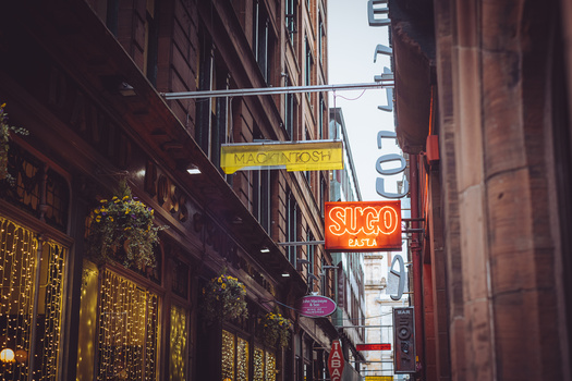 Neon signs illuminating a narrow urban street between tall buildings at dusk.