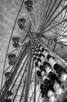 Upward view of a Ferris wheel with passenger cars and structural support cables in black and white.