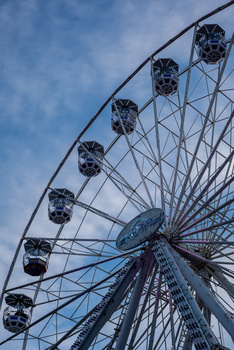 Ferris wheel shot from below against blue sky, capturing suspended gondolas and geometric steel framework.