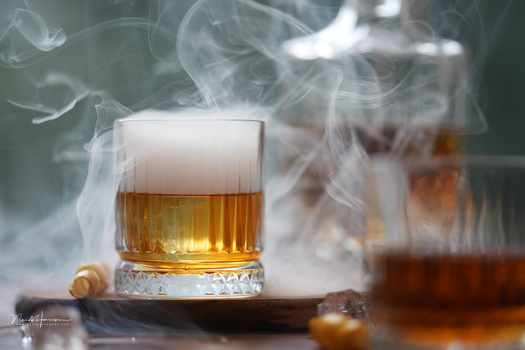 Whiskey glass with dramatic dry ice vapor and warm golden lighting against a dark background.