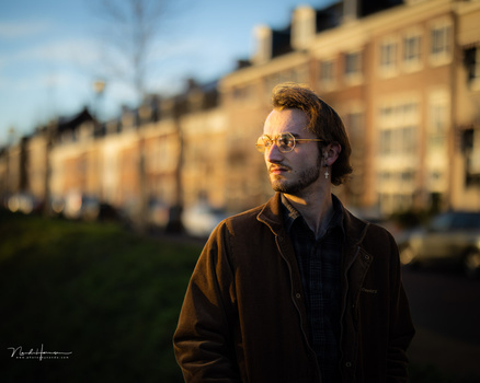 Man in brown jacket and glasses looking off-camera with golden hour sunlight on his face.