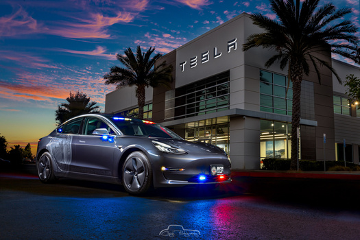 Tesla Model 3 with emergency lights activated in front of Tesla showroom at dusk.