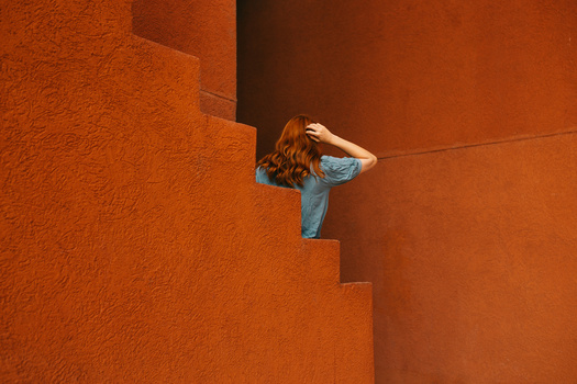Woman in blue shirt sitting on stepped terracotta wall, shading eyes with hand.