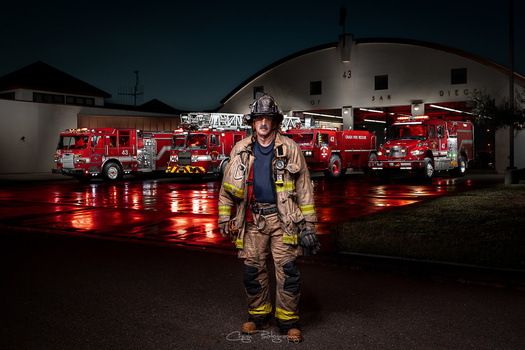Firefighter in full protective gear standing in front of illuminated fire trucks at night.