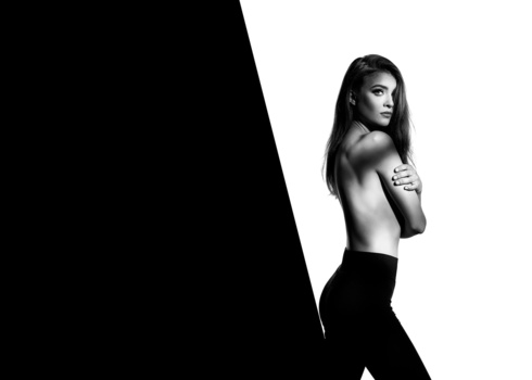 Black and white portrait of a woman with long dark hair, shot from behind with dramatic diagonal composition against contrasting light and dark backgrounds.