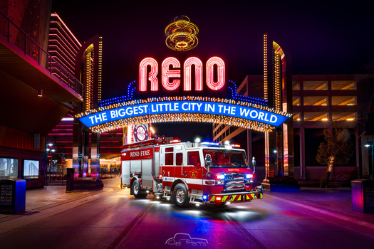 Fire truck parked beneath illuminated Reno casino sign at night.
