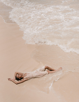Person lying on wet sand at the water's edge during golden hour.