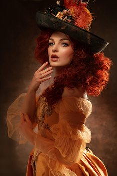 Woman with voluminous curled red hair wearing a black top hat and sheer golden overlay against a dark background.