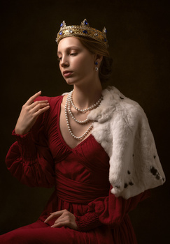 Woman wearing a golden crown, red velvet dress, and white fur stole against dark background.
