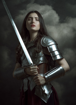 Woman in medieval armor holding a sword against a stormy sky backdrop.