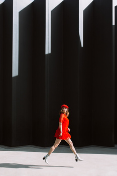 Woman in red dress jogging against dark geometric architecture with strong shadows.