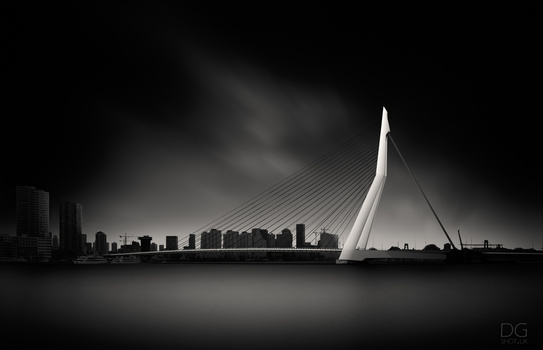 Modern cable-stayed bridge with white pylons spanning a river, flanked by urban skyline under dramatic storm clouds.