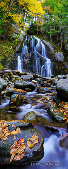 Multi-tiered waterfall cascading through forested landscape with moss-covered rocks and flowing stream.