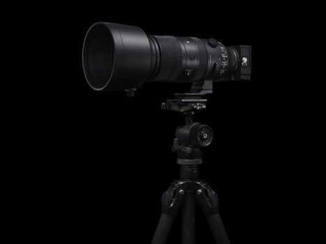 Professional telephoto lens mounted on tripod with ball head against black background.