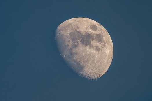 Waning gibbous moon against deep blue twilight sky, showing detailed surface features and craters.