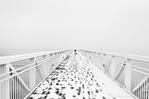Long wooden boardwalk stretching into fog with footprints in snow on the deck.