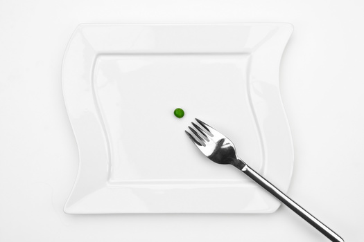 Single green pea on a white plate with a fork positioned beside it.
