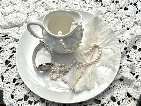Styled flat lay of pearl jewelry, white feathers, and accessories arranged on a ceramic plate.