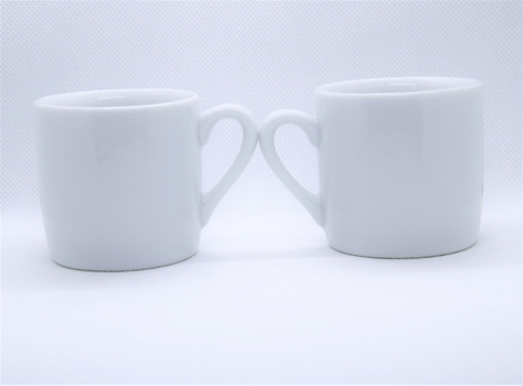 Two white ceramic mugs positioned face-to-face with handles meeting in the center against a light gray background.