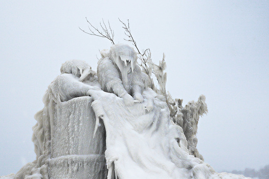 Lighthouse tower encased in thick ice and frozen spray during winter storm.