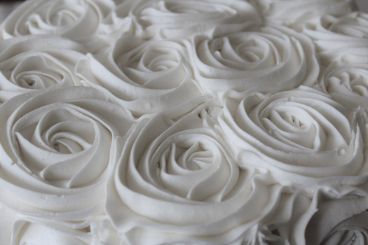 Close-up of white frosting piped into rose shapes on a cake surface.