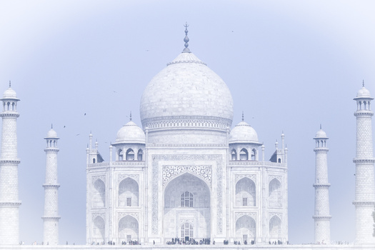 White marble mausoleum with large central dome and four minarets under hazy sky.