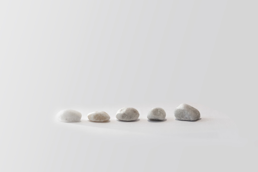 Five smooth stones arranged in a line on a neutral gray surface, progressively increasing in size from left to right.