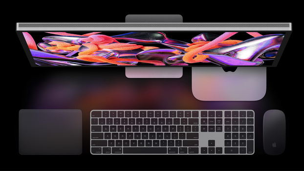 Overhead view of a Mac desktop setup with monitor, keyboard, mouse, and compact computer tower on dark surface.